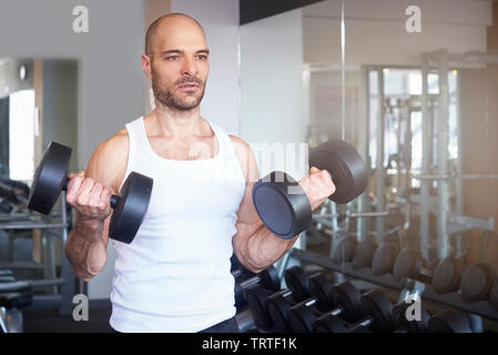 Close-up of man in the gym using barbells and doing dumbbell exercises to create more muscular body. Stock Photo
