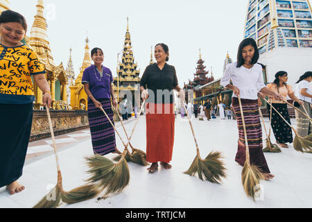 Yangon, Myanmar - March 2019: Burmese women swipe the floor with brooms in Buddhist Shwedagon pagoda temple complex. Stock Photo