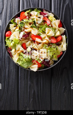 Delicious Italian pasta salad with avocado, strawberries, lettuce, dressed with balsamic sauce close-up on a plate on the table. Vertical top view fro Stock Photo