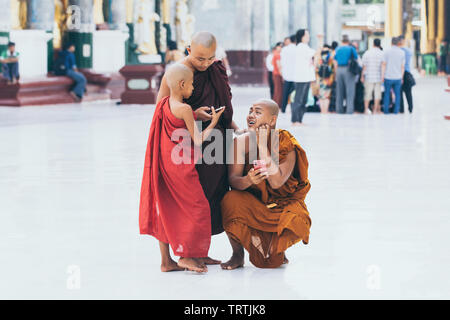 Yangon, Myanmar - March 2019: young Buddhist novice monks with gadgets in Shwedagon pagoda temple complex. Looking on telephone screen. Stock Photo