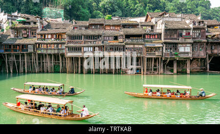 2 June 2019, Fenghuang China : Traditional wooden boats full of tourists crusing on Tuojiang river and old traditional houses on riverside in Fenghuan Stock Photo
