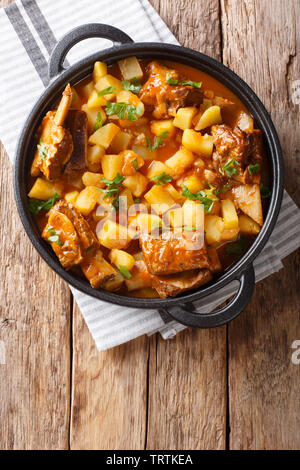 Slow cooked short beef ribs with potatoes in a spicy sauce close-up in a pot on the table. Vertical top view from above Stock Photo