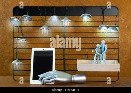 A black shelf in front of real rust. Mine lights shine. Two robot figures hugging each other. The man points to a tablet. A free space on a tablet lea Stock Photo