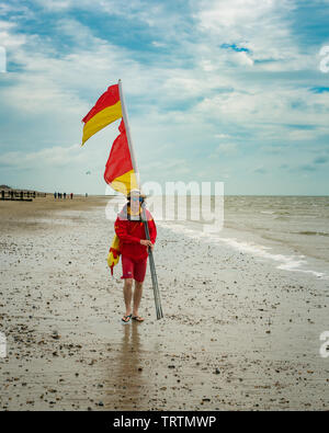 Life guard walking along a beach carrying flags