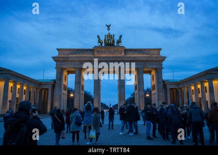 Many tourists taking photos and hanging out at the famous and illuminated neoclassical Brandenburg Gate (Brandenburger Tor) in Berlin, Germany at dusk Stock Photo