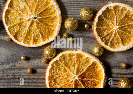 Christmas composition with three dried oranges and golden glitter balls on wooden background - close-up Stock Photo
