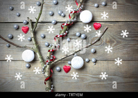 Christmas tree concept with leafless tree branches, snow flakes, white baubles, red hearts, glitter globules and bead chain on wooden background Stock Photo