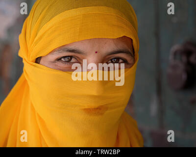 Young Indian woman covers her hair and lower face with a semi-sheer, yellow dust veil. Stock Photo