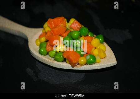 pieces of carrots, corn and peas on wooden spoon with dark background Stock Photo