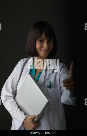 Indian female doctor holding a laptop and giving thumbs up Stock Photo