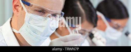 Panorama of male scientist, scientific researcher or doctor looking at a test tube of clear liquid in a medical research lab or laboratory Stock Photo