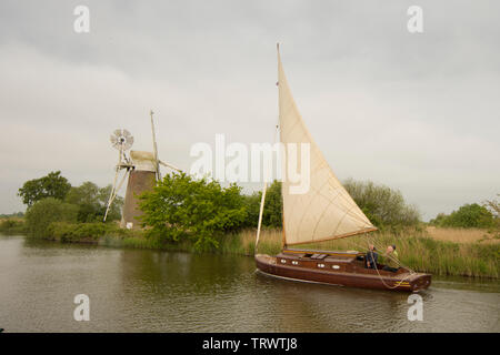 Three men in sailing boat on River Ant sailing in front of Turf Fen Drainage Mill, How Hill, Norfolk Broads, UK, May Stock Photo