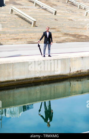 Adult man in formal clothes while walking on promenade holding an umbrella. Stock Photo