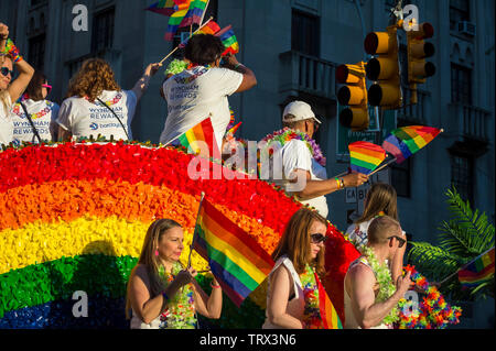 NEW YORK CITY - JUNE 25, 2017: Participants wearing Wyndham and Barclays shirts wave flags on a float with a rainbow arc at the gay Pride Parade. Stock Photo