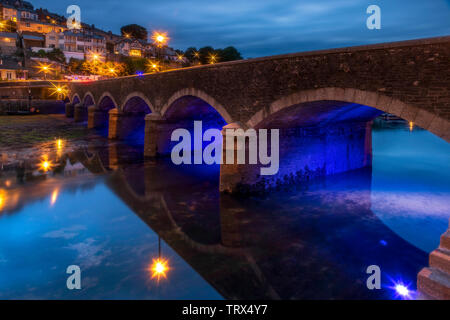 After another chilly overcast day the lights flicker on as the daylight gives way to dusk in the historic fishing port of Looe in Cornwall. Stock Photo