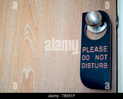 Closed wooden door of hotel room with please do not disturb sign hanging on the stainless steel door knob with copy space. Stock Photo