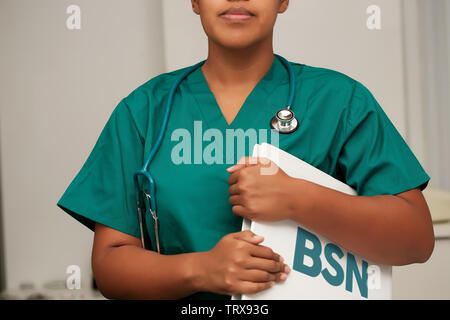 A nurse enrolled in a Bachelor of Science in Nursing degree program, holding a binder in her arms and wearing a stethoscope. Stock Photo