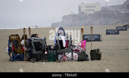 Friends Gathered On Ocean Beach With Lawn Chairs And Tiki