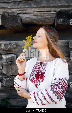 Portrait of Beautiful girl with long hair in white ethnic shirt with flower bouquet. Traditional village of Eastern Europe. National architecture muse Stock Photo