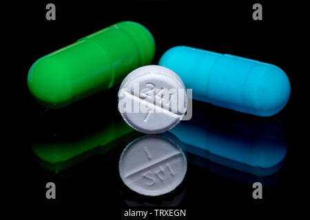 Macro Image of a green pill, blue pill, and a white pill on a reflective black surface. pharmaceuticals on display. Stock Photo