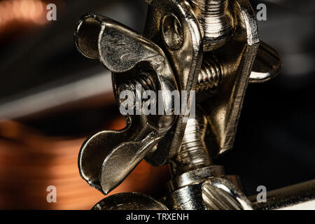 A wing nut and thumb screw securing a steel ball joint on a pice of shop equipment.  Helping hands tools are often used in soldering, macro photograph Stock Photo