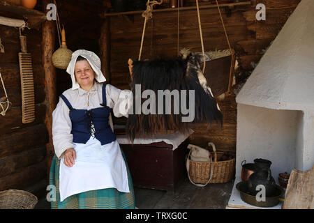 Woman in traditional swedish clothes rocks a cradle with a baby. Reconstruction of life in Sweden of 18th century Stock Photo
