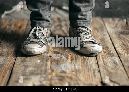 Male beggar wearing torn sneakers seeking food or money from human kindness on the wooden floor at public path way, street walkway. Homeless poor in the city. Problems with finance, place of residence. Stock Photo