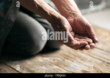 Male beggar hands seeking money, coins from human kindness on the wooden floor at public path way or street walkway. Homeless poor in the city. Problems with finance, place of residence. Stock Photo