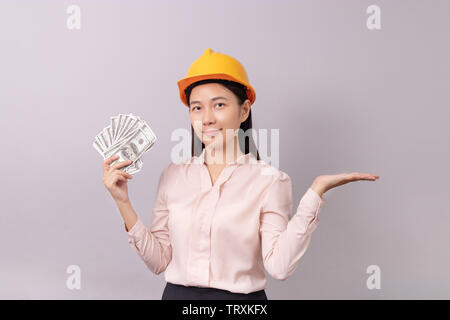 loans for real estate concept, woman with yellow helmet holding banknote money in right hand and open the empty palm of the left hand Stock Photo