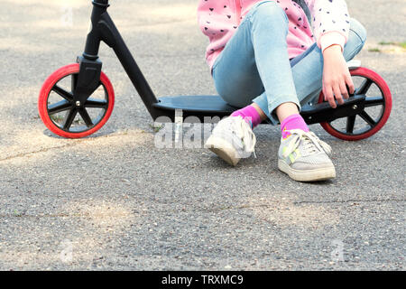 Child in blue pants and sneakers sitting on kick scooter. Kids play outdoors. Active leisure and outdoor sport for children. Stock Photo