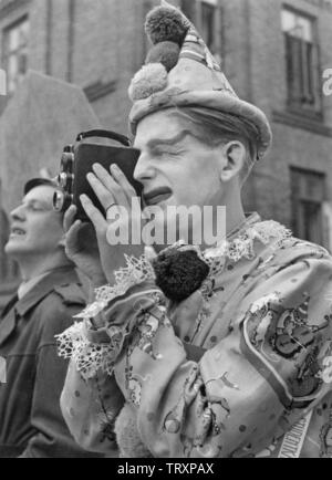 Amateur filming in the 1940s. A man dressed as a clown filming something interesting. Film cameras at this time often used Kodak standard 8 film. A 16 mm film where you first filmed on one half and the turned the roll of film to film on the other. During developing the film was cut in half and becam an 8 mm film with no sound. The film cameras was not battery operated and you had to wind them up as you do with a clock to make them work. Stock Photo