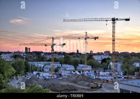 Uebersichtsaufnahme einer Baustelle in Essen NRW zur blauen Stunde mit drei in den Himmel ragenden Baukraenen. Stock Photo