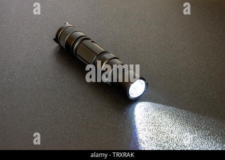 Metallic black LED flashlight on a black background. Light beam on textural background Stock Photo