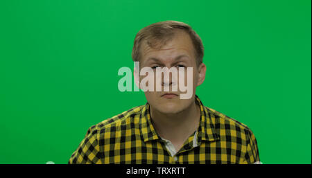 Handsome young man in the yellow shirt without glasses sees poorly on the chroma key background. Poor eyesight concept. Green screen. Stock Photo