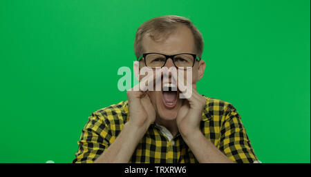 Handsome young man in the yellow shirt got angry and started shouting loudly on the chroma key background. Green screen. Stock Photo