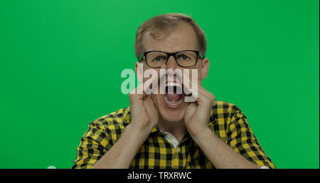 Handsome young man in the yellow shirt got angry and started shouting loudly on the chroma key background. Green screen. Stock Photo