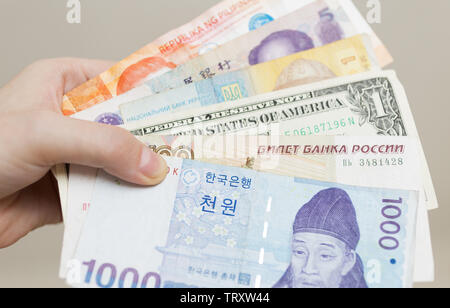 A hand holding money banknotes of different countries: Korean won, Russian rouble, Dollar USA, Chinese RMB yuan and ukraine grivna Stock Photo