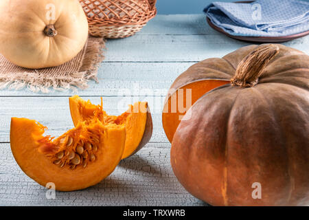 Two pumpkins with natural imperfections and two bright orange slices with seeds on blue wooden surface. Cloth and basket at background. Selective focu Stock Photo