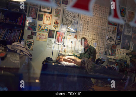 Tattoo artist tattooing the back of a woman in his shop in Amsterdam Stock Photo