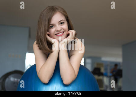 Smiling young caucasian woman girl on blue gymnastic ball at the gym, doing workout or yoga pilates exercise Stock Photo