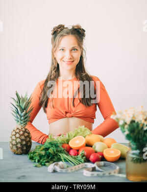 A young smiling woman is standing next to vegetables, fruits and a measuring tape on a table. The concept of diet and healthy eating. Stock Photo