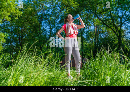 a young jogger in nature drinks from a blue water bottle Stock Photo