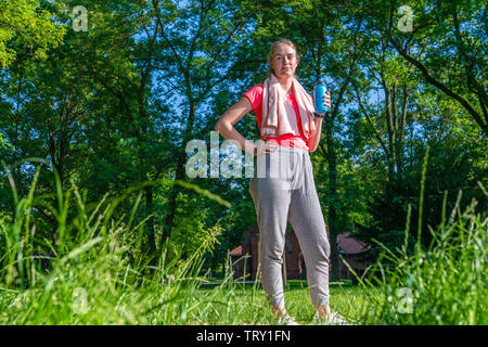 a young sportswoman in nature holds a bottle of drink in her hand and looks into the camera Stock Photo