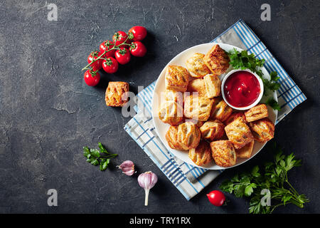 overhead view of freshly baked Puff pastry rolls with minced chicken meat  and mushrooms served with ketchup and parsley on a white plate on a concret Stock Photo