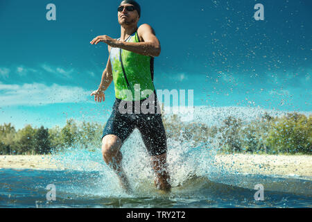 Professional triathlete swimming in river's open water. Man wearing swim equipment practicing triathlon on the beach in summer's day. Concept of healthy lifestyle, sport, action, motion and movement. Stock Photo