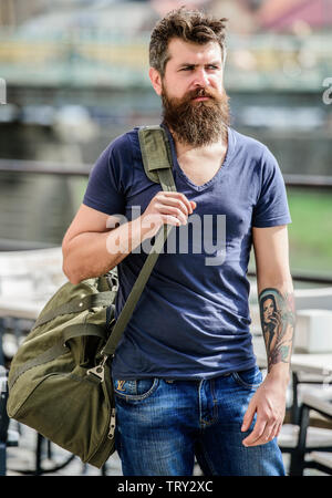 Travelling and vacations concept. Muscular man with beard and mustache carrying big sporty bag. Tourist explore city with luggage. Heavy bag on his shoulder. Carry things in big bag on shoulder Stock