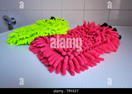 A neon yellow and a red wash mitt lying on white background in the bathroom Stock Photo
