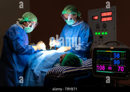 Electrocardiogram in hospital surgery operating emergency room showing patient heart rate with blur team of surgeons in background. Health and medicin Stock Photo