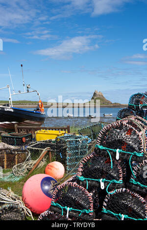 A Fishing Boat and a Pile of Lobster and Crab Pots Frame Lindisfarne Castle on Holy Island Northumberland England United Kingdom UK Stock Photo
