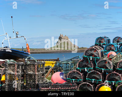 A Fishing Boat and a Pile of Lobster and Crab Pots Frame Lindisfarne Castle on Holy Island Northumberland England United Kingdom UK Stock Photo